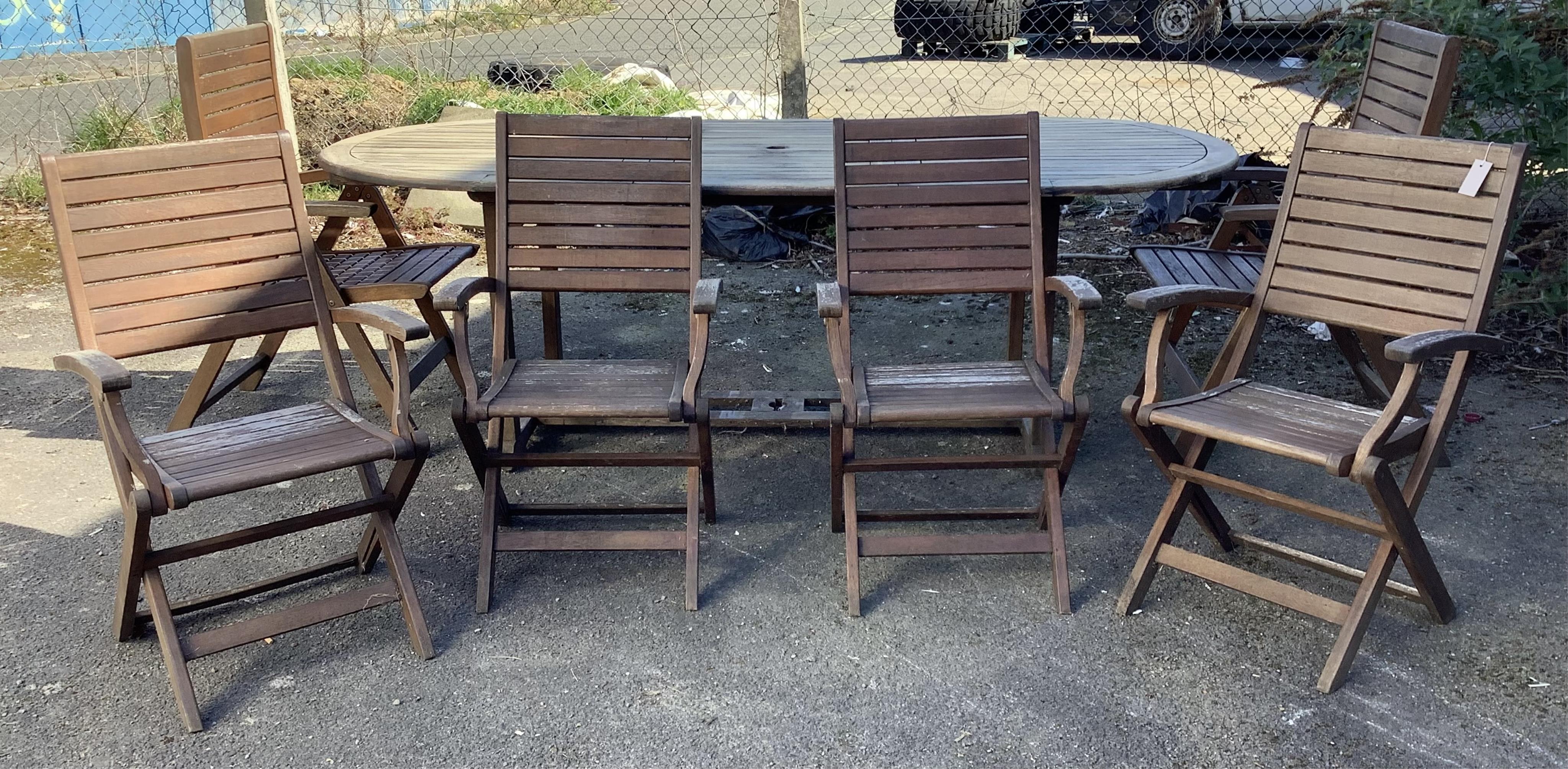A weathered oval teak extending garden table, width 230cm extended, depth 102cm, height 77cm and six weathered teak folding garden chairs. Condition - fair